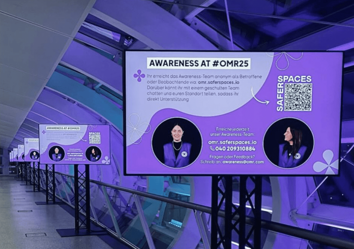 Digitale Infotafeln mit lila Hintergrund informieren über Awareness bei #OMR25 und bieten Kontaktmöglichkeiten für Unterstützung.