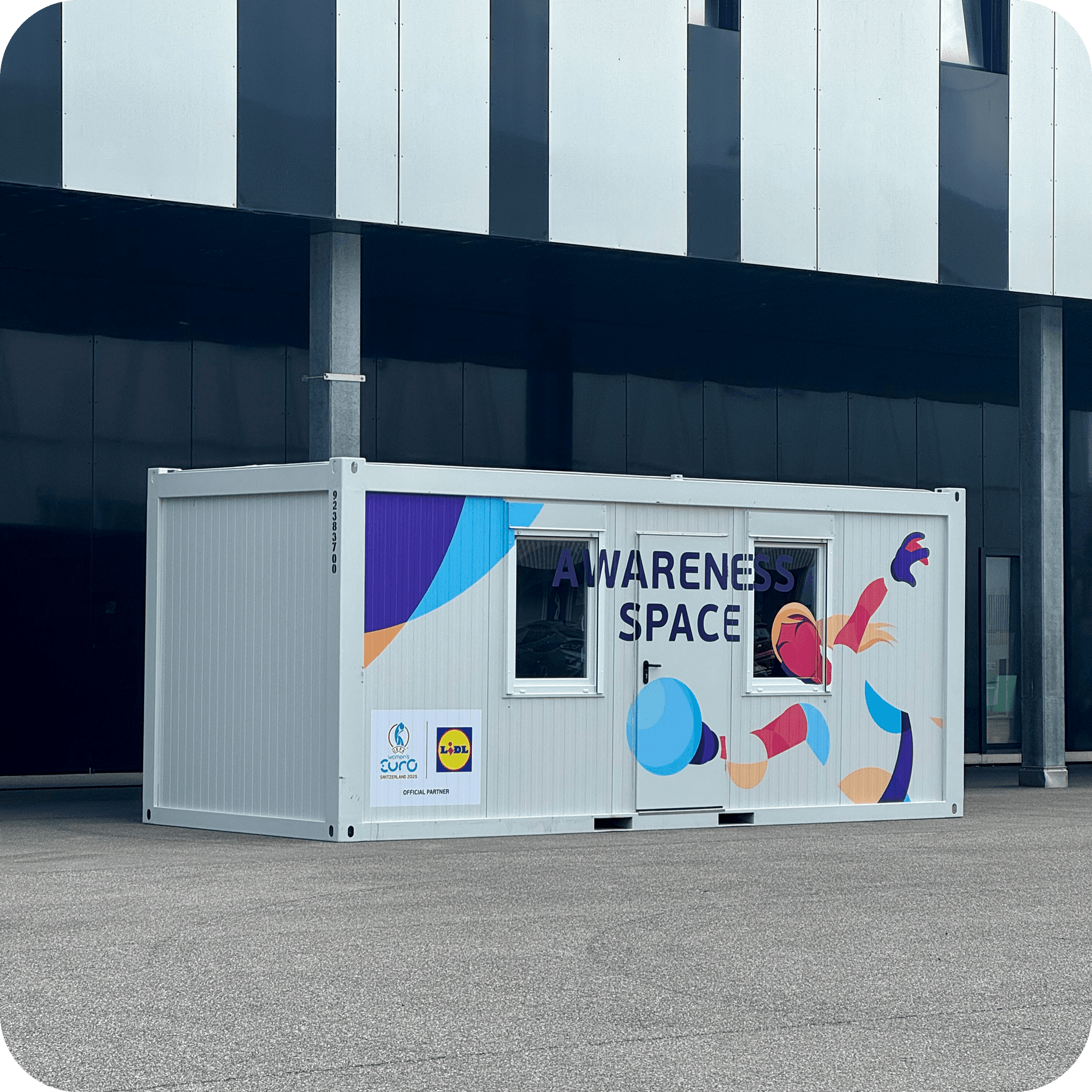 White container with colorful graphic and text 'AWARENESS SPACE' in front of a modern building.