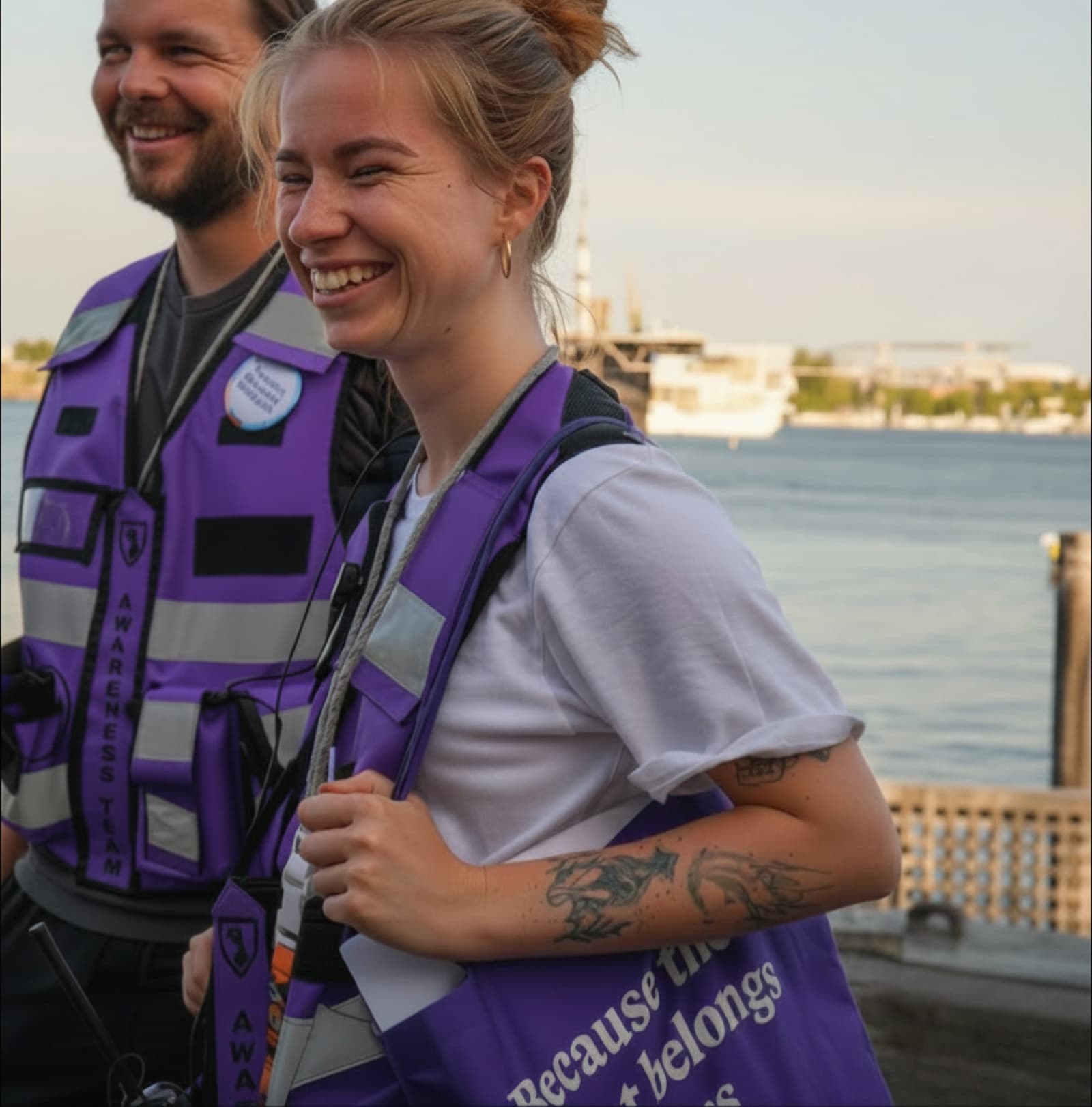 Zwei Mitglieder des Awareness-Teams in lila Westen lächeln am Hafen.